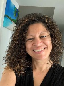 Woman with dark curly fair smiling wearing a black top and necklace